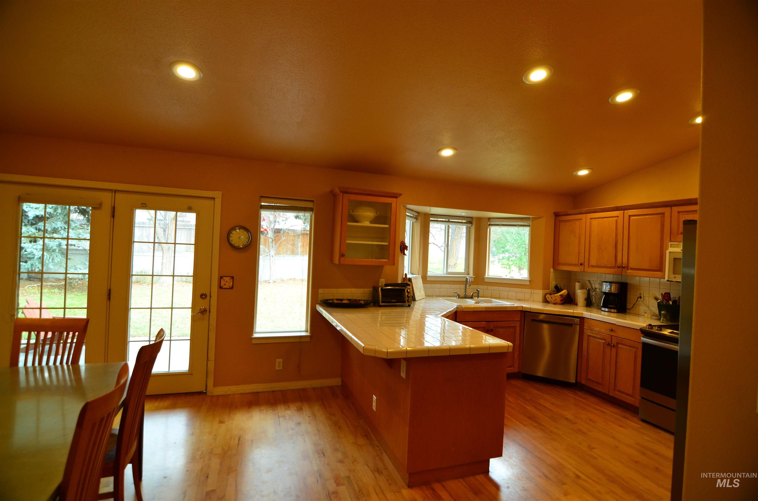 690 Granite Way Boise, ID 83712 - Photo 5 of 30 Kitchen with tile countertops, a breakfast bar, appliances with stainless steel finishes, a peninsula, and brown cabinets