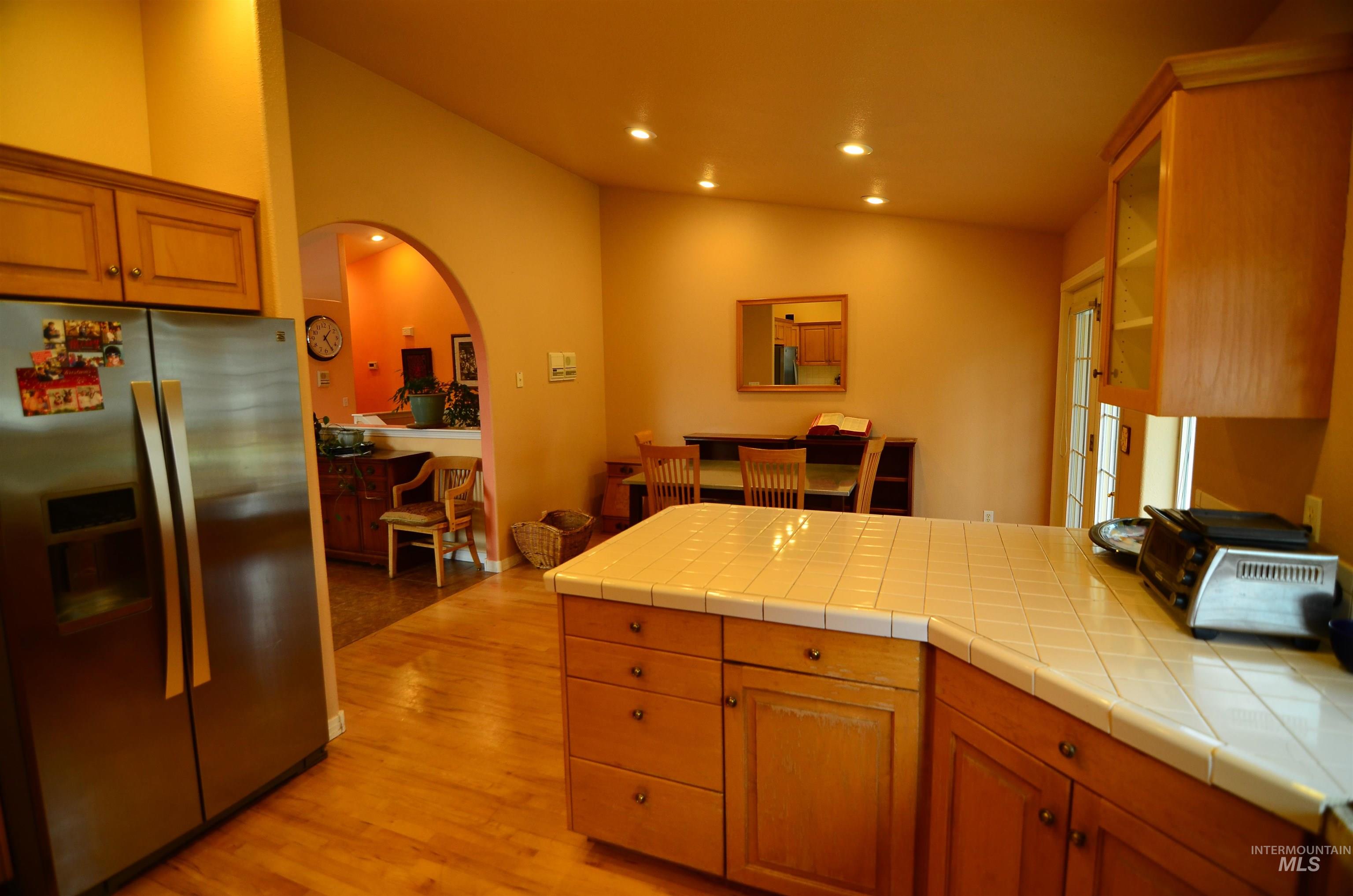 690 Granite Way Boise, ID 83712 - Photo 8 of 30 Kitchen featuring stainless steel fridge, tile countertops, lofted ceiling, arched walkways, and brown cabinets