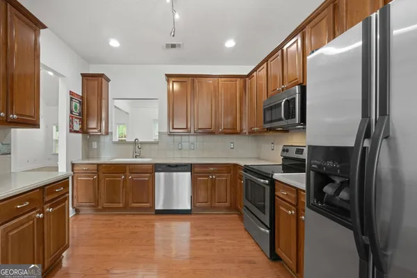 a large kitchen with stainless steel appliances granite countertop a stove top oven a sink dishwasher a refrigerator and cabinets with wooden floor