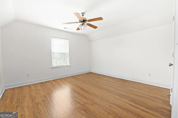 an empty room with wooden floor fan and windows