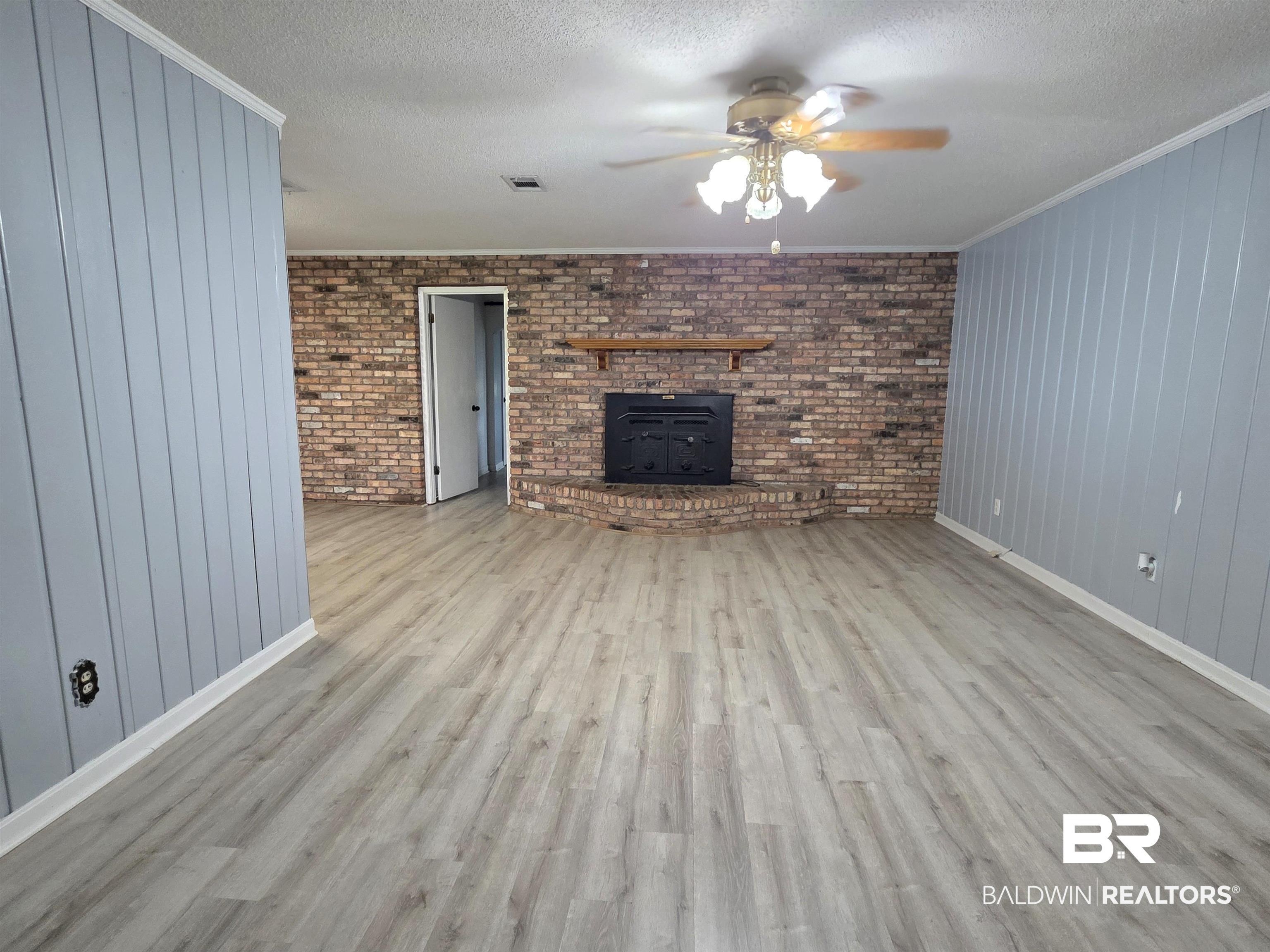 558 Stanton Road Atmore, AL 36502 - Photo 6 of 29 Spacious living area featuring wood-finish flooring, brick accent wall with fireplace, wood mantel, and a ceiling fan with integrated lighting