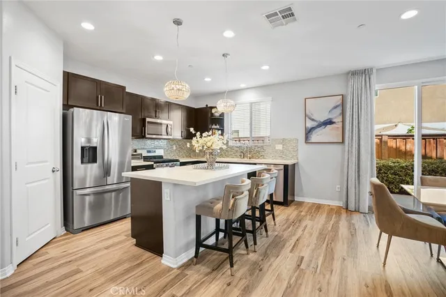 a kitchen with stainless steel appliances kitchen island granite countertop a refrigerator a stove a sink a dining table and chairs with wooden floor
