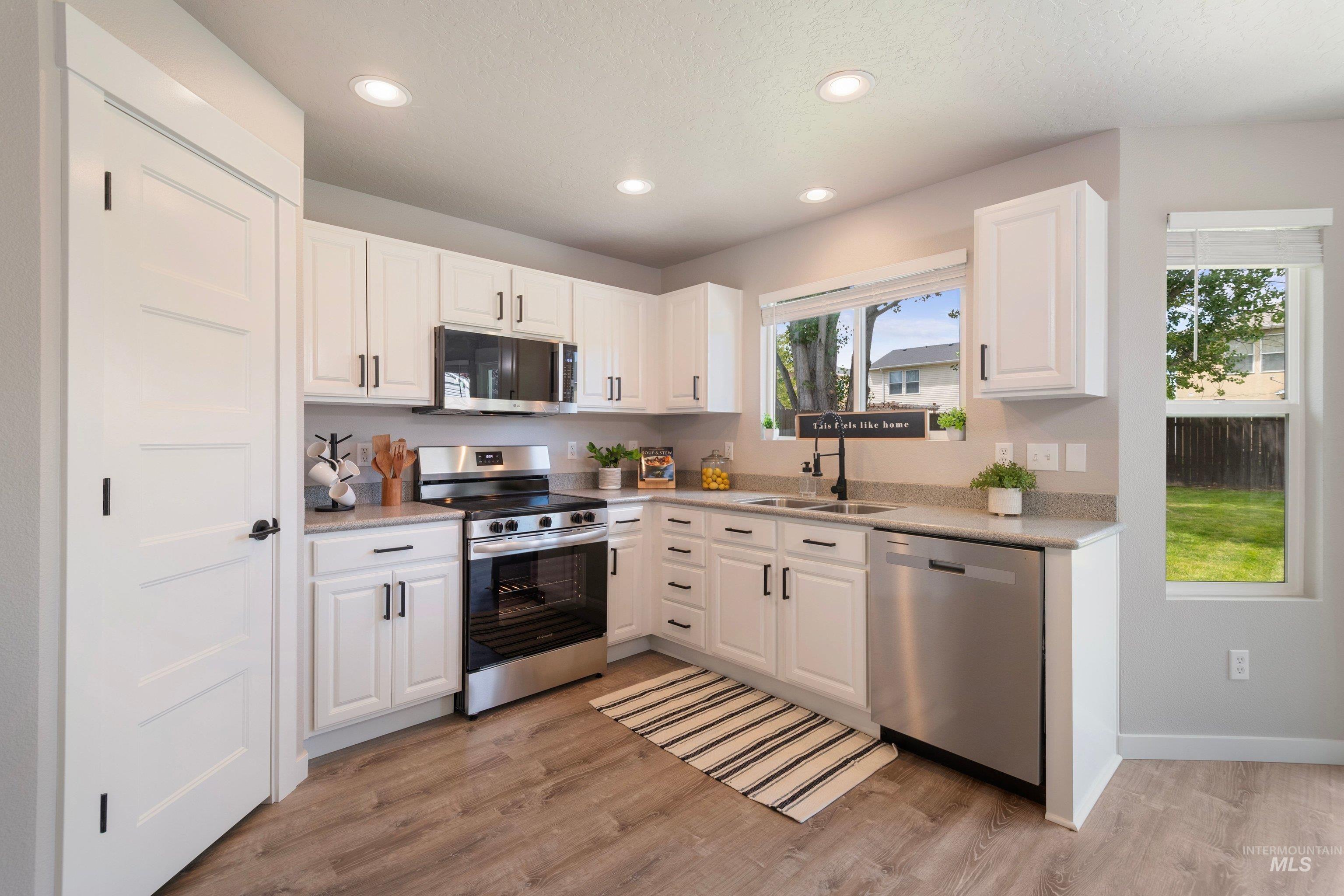 16759 Abram Avenue Caldwell, ID 83607 - Photo 12 of 33 Kitchen featuring white cabinetry, stainless steel appliances, wood-finish flooring, recessed lighting, and a double basin sink
