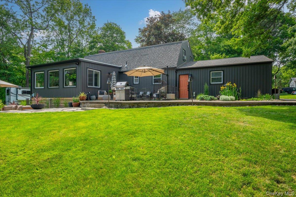 13 Jacks Pond Road Newburgh, NY 12550 - Photo 28 of 44 Expansive rear lawn featuring a stone patio, vibrant perimeter landscaping, and mature surrounding trees