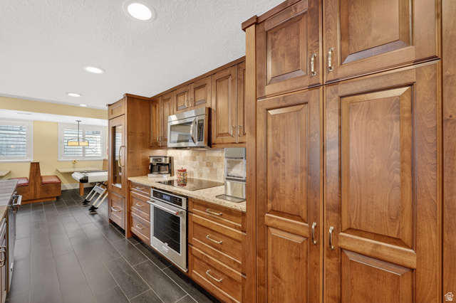 714 Draper Heights Way Draper, UT 84020 - Photo 54 of 88 Kitchen featuring wood finish cabinetry, light stone countertops, stainless steel appliances, decorative backsplash, and hanging light fixtures