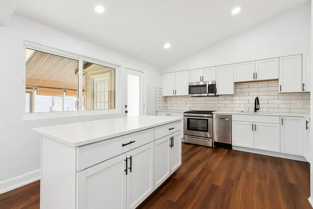 a kitchen with stainless steel appliances a stove top oven a sink dishwasher and a refrigerator with wooden floor