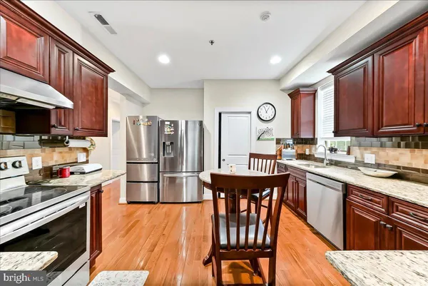 a kitchen with stainless steel appliances granite countertop a refrigerator a stove top oven a sink dishwasher and white cabinets with wooden floor