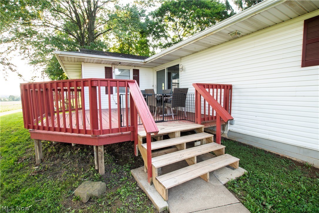 1757 Pleasant Valley Road Northeast New Philadelphia, OH 44663 - Photo 9 of 33 Outdoor wood deck with red railing, featuring direct access to a sliding glass door and a concrete pathway leading to wood steps