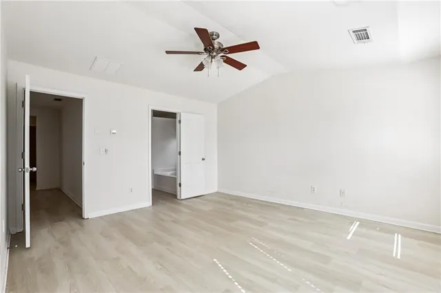 an empty room with wooden floor fan and windows