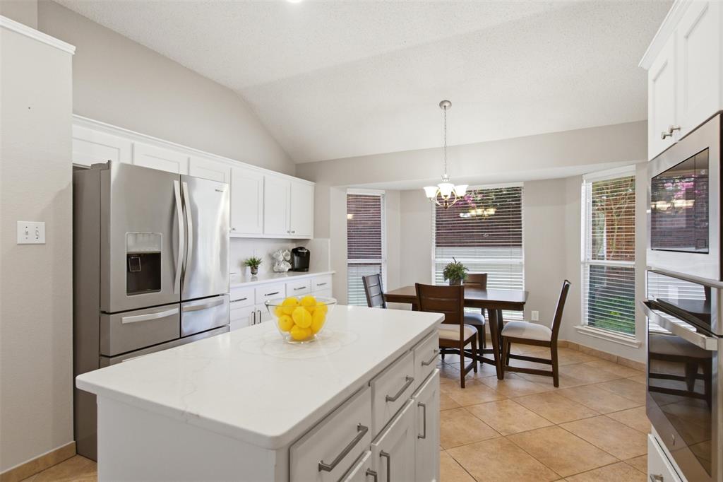 4218 Glistening Spring Rowlett, TX 75088 - Photo 14 of 39 Kitchen featuring a central island with a light-colored countertop, white cabinetry with silver hardware, stainless steel refrigerator, built-in oven, and tile flooring