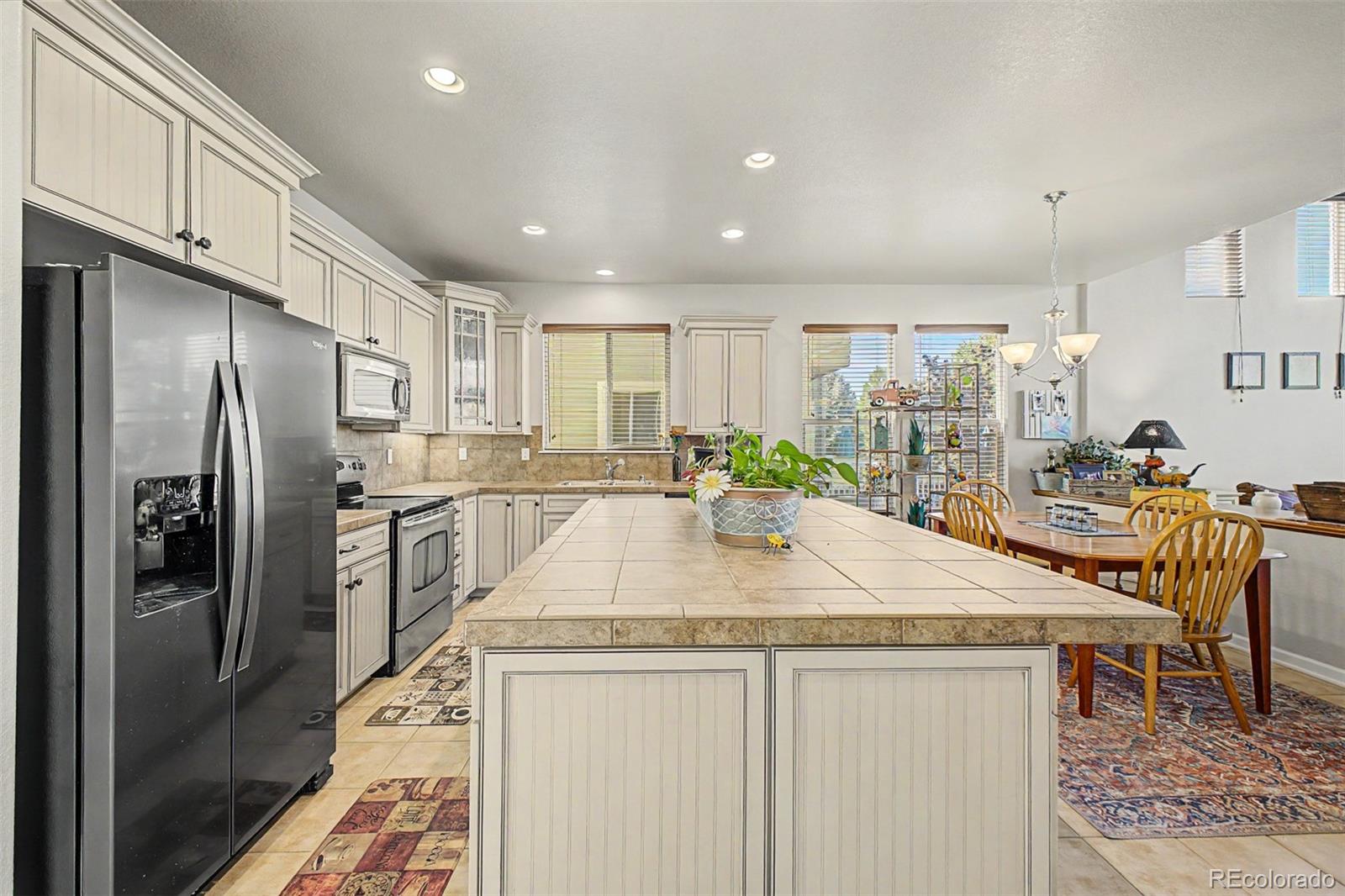 3343 Fantasy Place Castle Rock, CO 80109 - Photo 8 of 50 a kitchen with stainless steel appliances kitchen island granite countertop a refrigerator a sink a stove and chairs with wooden floor