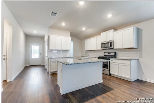 a kitchen with kitchen island granite countertop a sink cabinets and wooden floor