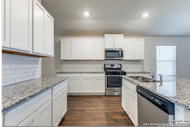 a kitchen with stainless steel appliances granite countertop white cabinets granite counter tops and a hard wood floors