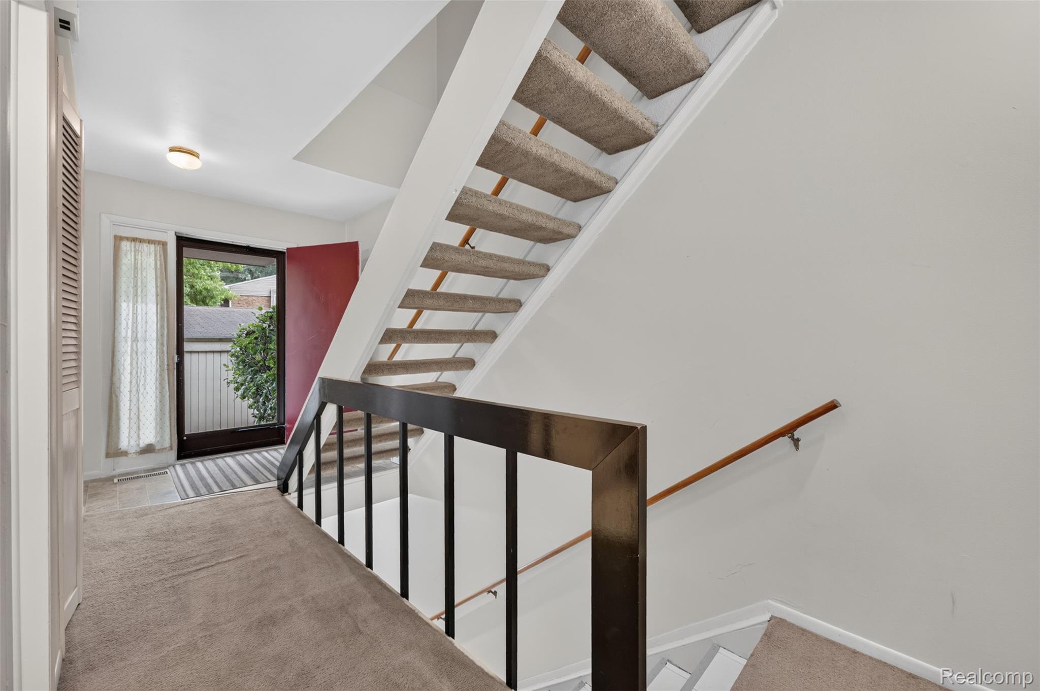 1439 Oakbrook E Drive Rochester, MI 48307 - Photo 28 of 68 Entryway with a solid red door, a staircase with carpeted treads, and a dark metal railing