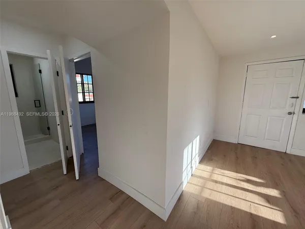 a view of an empty room with wooden floor and a hallway