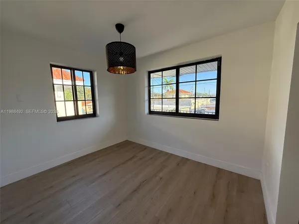 an empty room with wooden floor chandelier fan and windows
