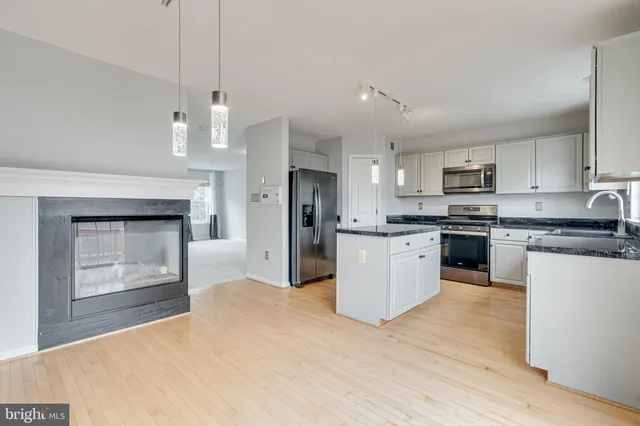 a kitchen with stainless steel appliances granite countertop a stove a sink dishwasher a refrigerator and white cabinets with wooden floor