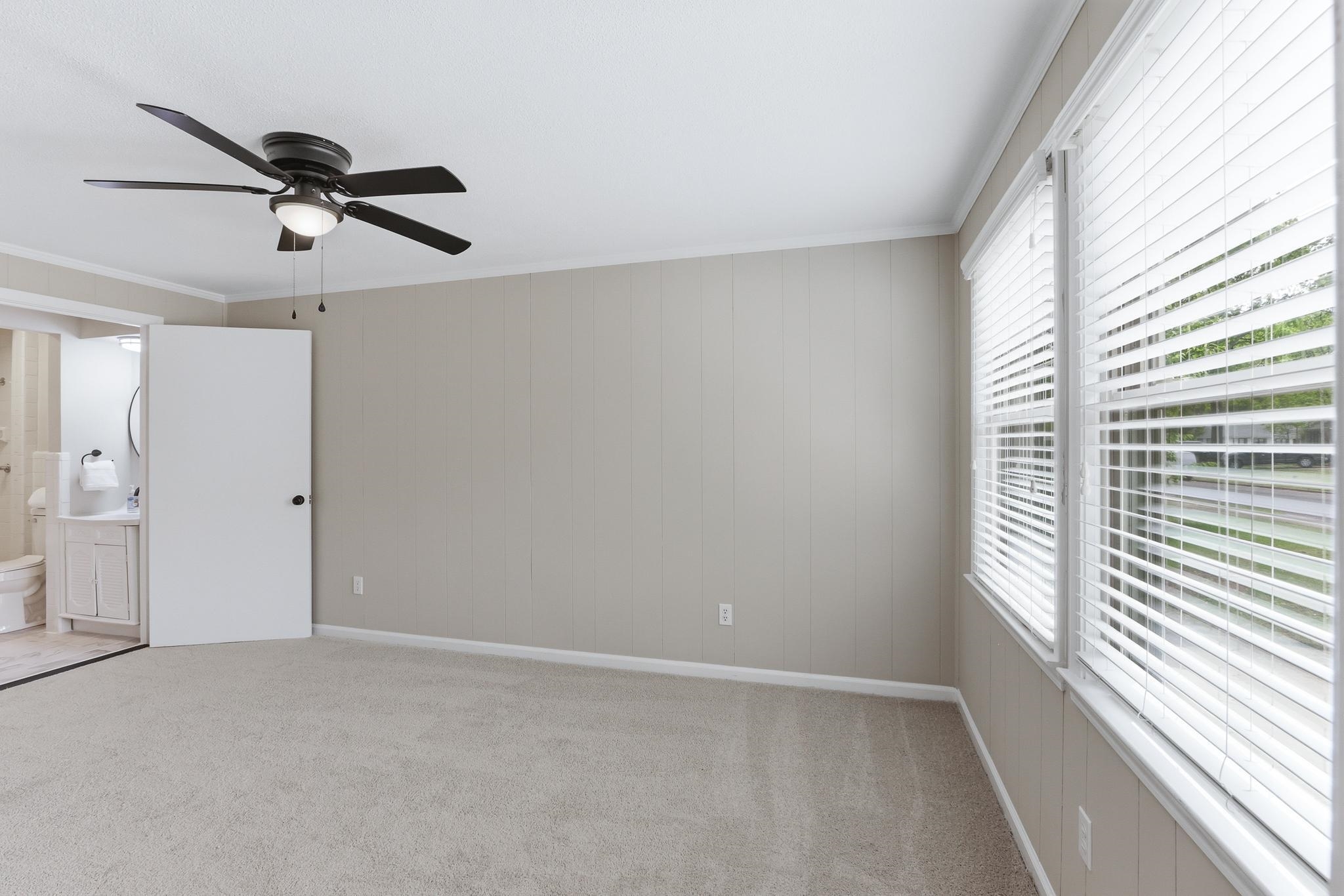312 Fernway Road Memphis, TN 38117 - Photo 6 of 38 Unfurnished bedroom featuring light colored carpet, ornamental molding, wooden walls, a ceiling fan, and connected bathroom