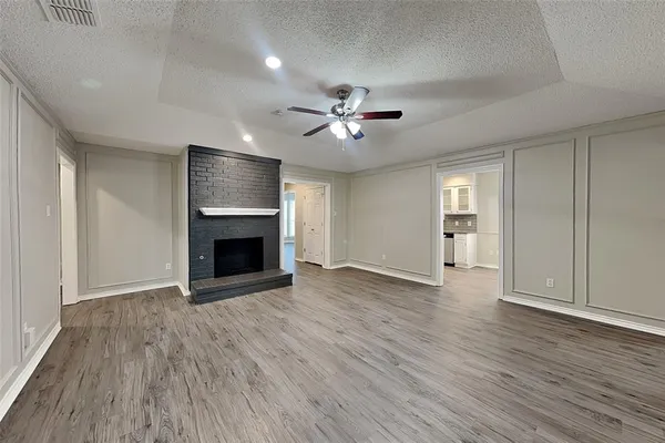 an empty room with wooden floor a ceiling fan a fireplace and windows