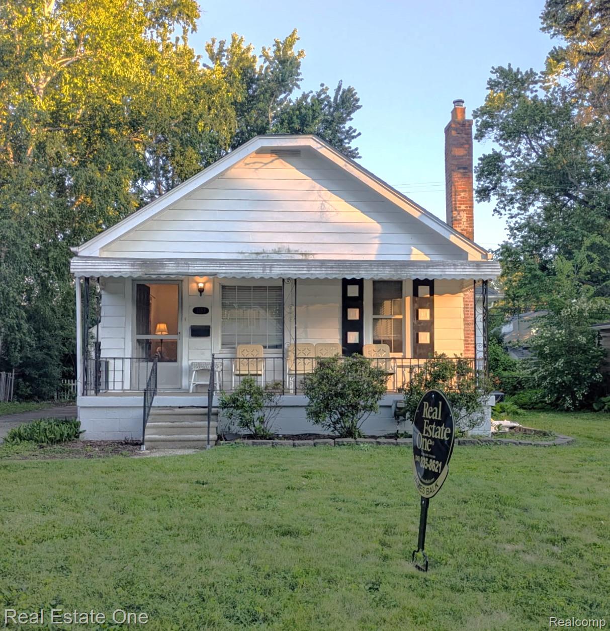 Traditional bungalow featuring white siding, a covered front porch, and a brick chimney