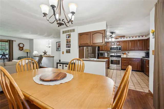 a dining room with kitchen island stainless steel appliances a table chairs and a chandelier