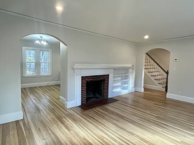 an empty room with wooden floor fireplace and windows