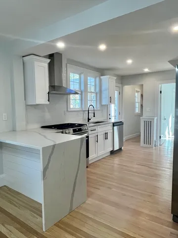 a kitchen with stainless steel appliances granite countertop a stove top oven a sink dishwasher and white cabinets with wooden floor