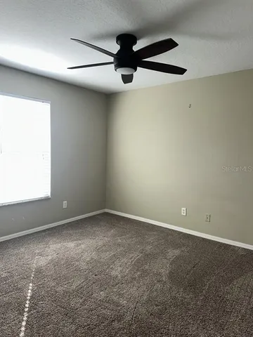 an empty room with a chandelier fan and windows