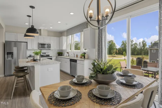 a kitchen with stainless steel appliances granite countertop a stove a refrigerator a sink a dining table and chairs with wooden floor