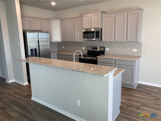 a kitchen with stainless steel appliances granite countertop a refrigerator a stove a sink and white cabinets with wooden floor