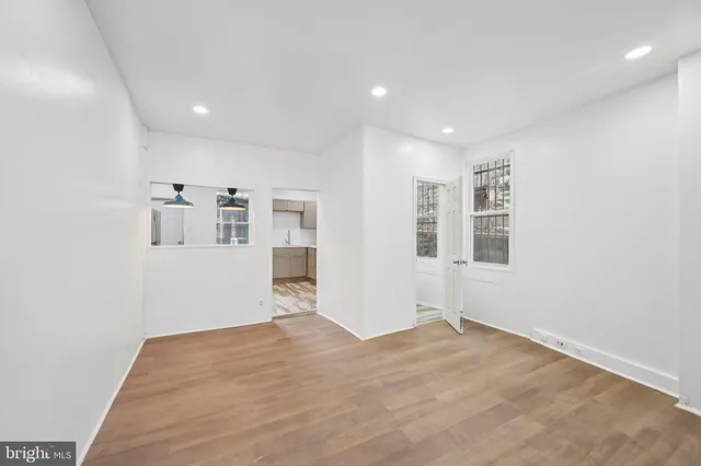 a view of empty room with wooden floor and kitchen
