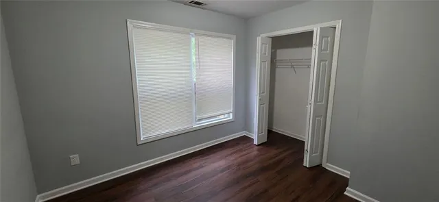 an empty room with wooden floor closet and windows