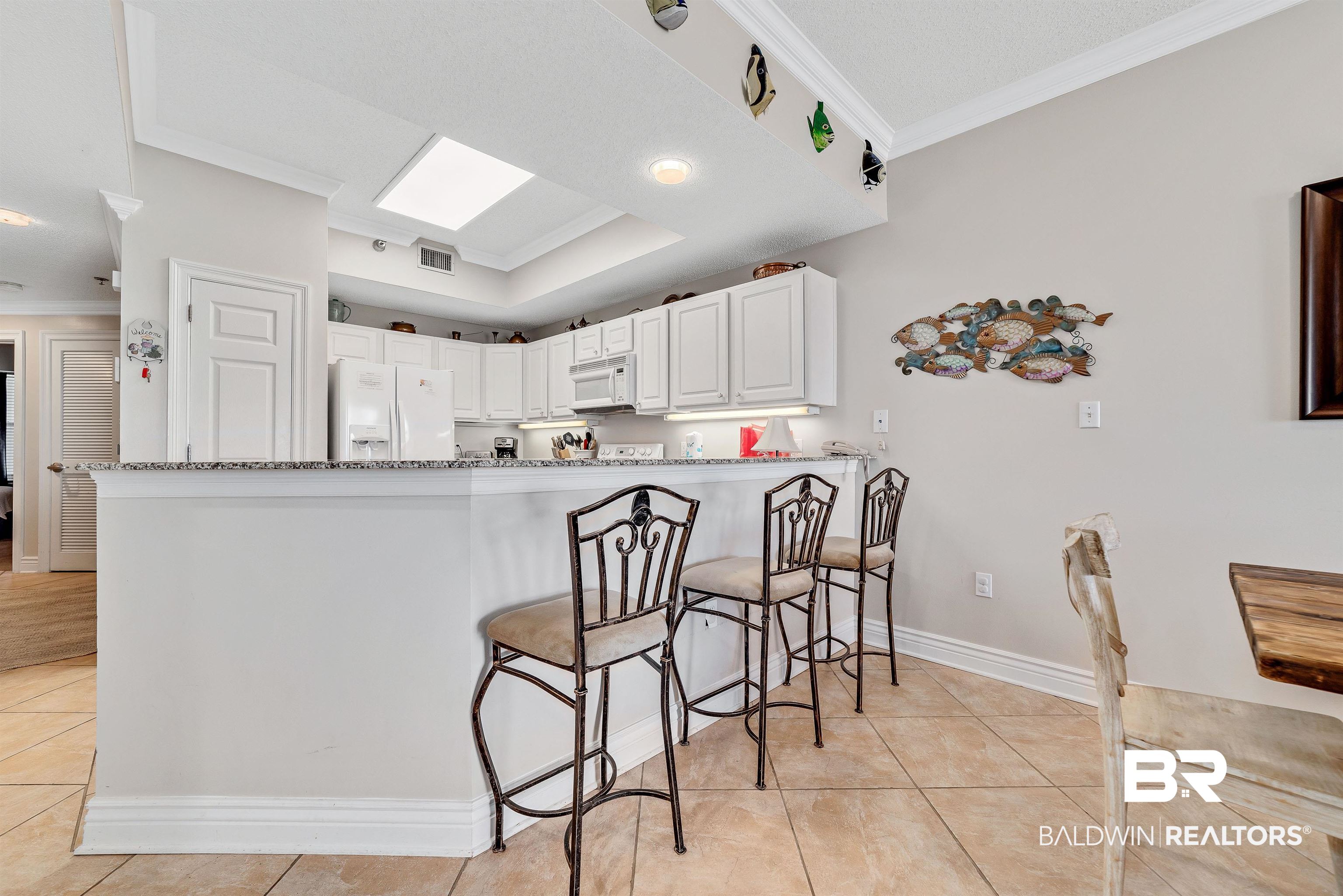 Kitchen featuring light tile patterned floors, ornamental molding, light stone countertops, white appliances, and a peninsula
