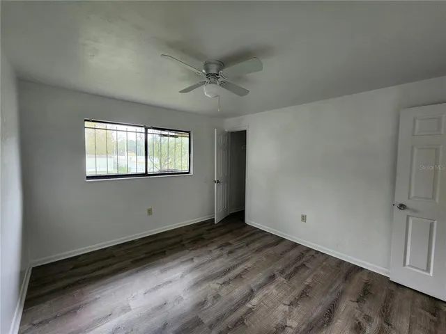 an empty room with wooden floor ceiling fan and windows
