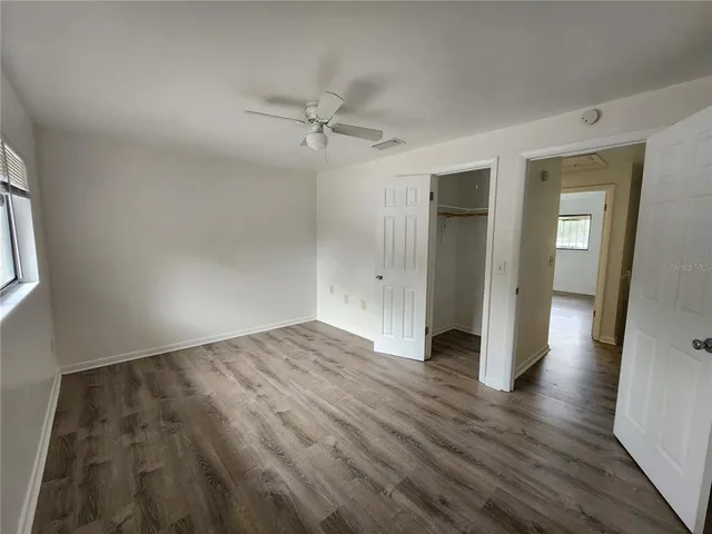 an empty room with wooden floor closet and windows