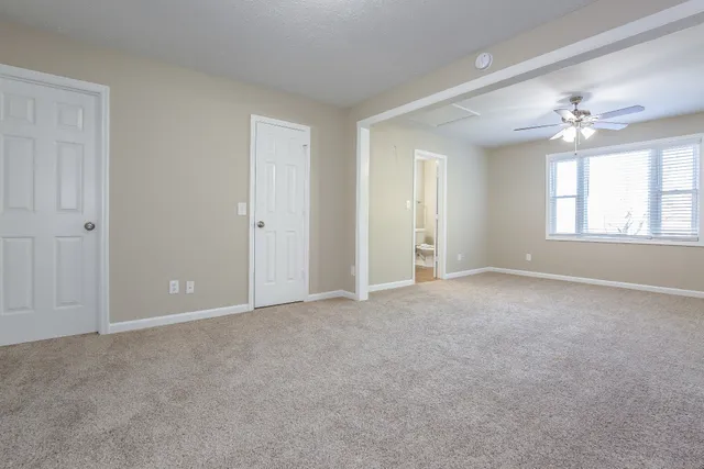 an empty room with chandelier fan and windows