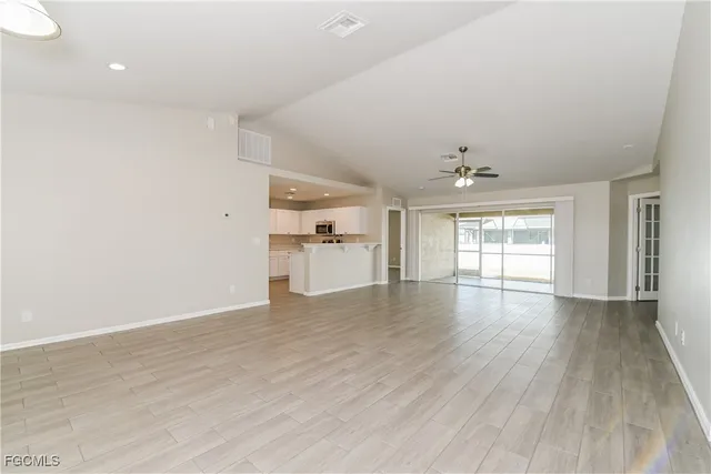 a view of empty room with wooden floor and kitchen view
