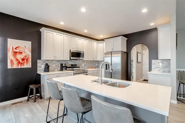 a kitchen with stainless steel appliances kitchen island granite countertop a stove a sink a refrigerator and white cabinets with wooden floor