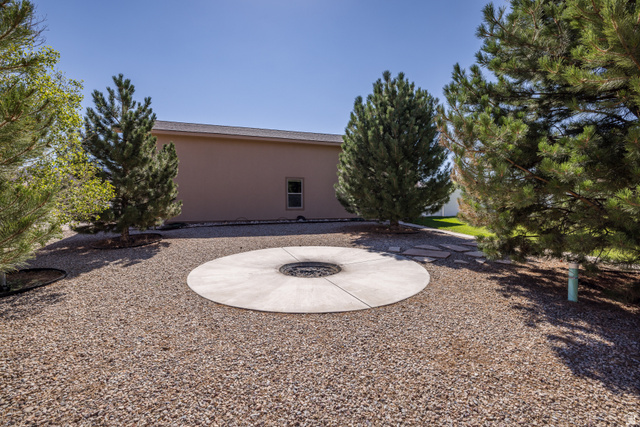 4635 East Sunny Acres Lane Moab, UT 84532 - Photo 26 of 56 Gravel landscaping featuring a circular concrete patio with a built-in fire pit, surrounded by mature evergreen trees
