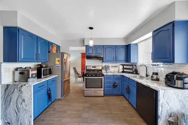 a kitchen with stainless steel appliances granite countertop a stove top oven a sink dishwasher and a refrigerator with wooden cabinets