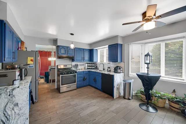 a kitchen with stainless steel appliances granite countertop a refrigerator a sink dishwasher a stove a dining table and chairs with wooden floor