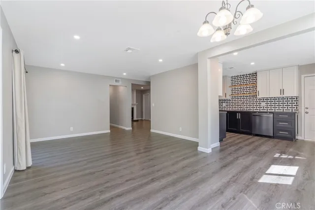 a view of a livingroom with a chandelier wooden floor and a kitchen