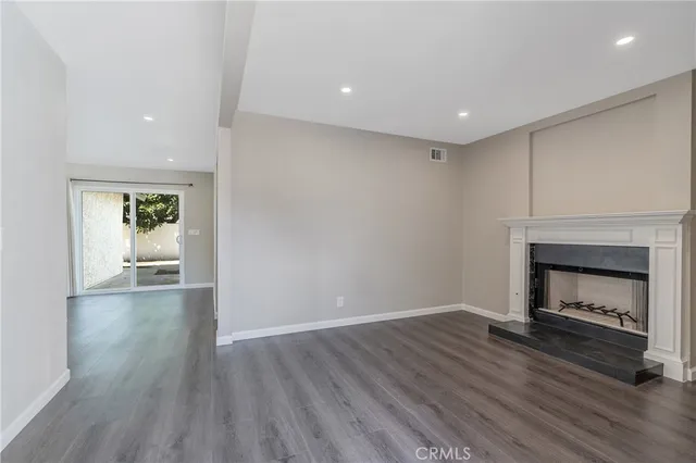 a view of an empty room with wooden floor fireplace and a window