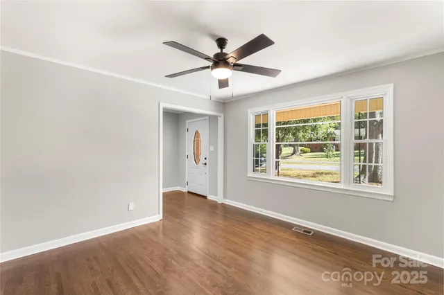 an empty room with wooden floor fan and windows