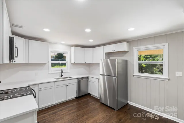 a kitchen with stainless steel appliances a sink a stove a refrigerator cabinets and a window