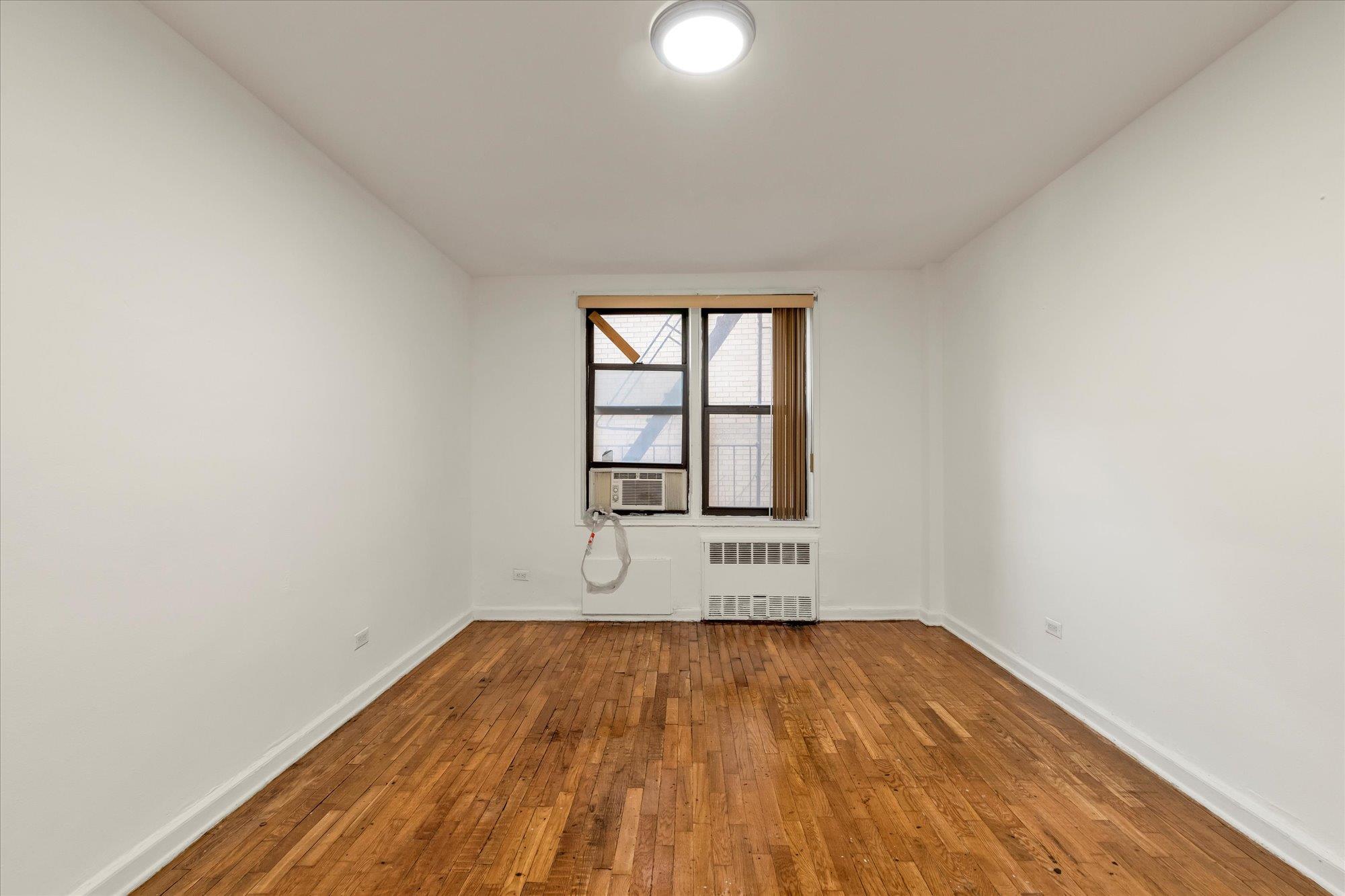 141-05 Pershing Crescent, Unit 117 Queens, NY 11435 - Photo 13 of 16 an empty room with wooden floor and windows
