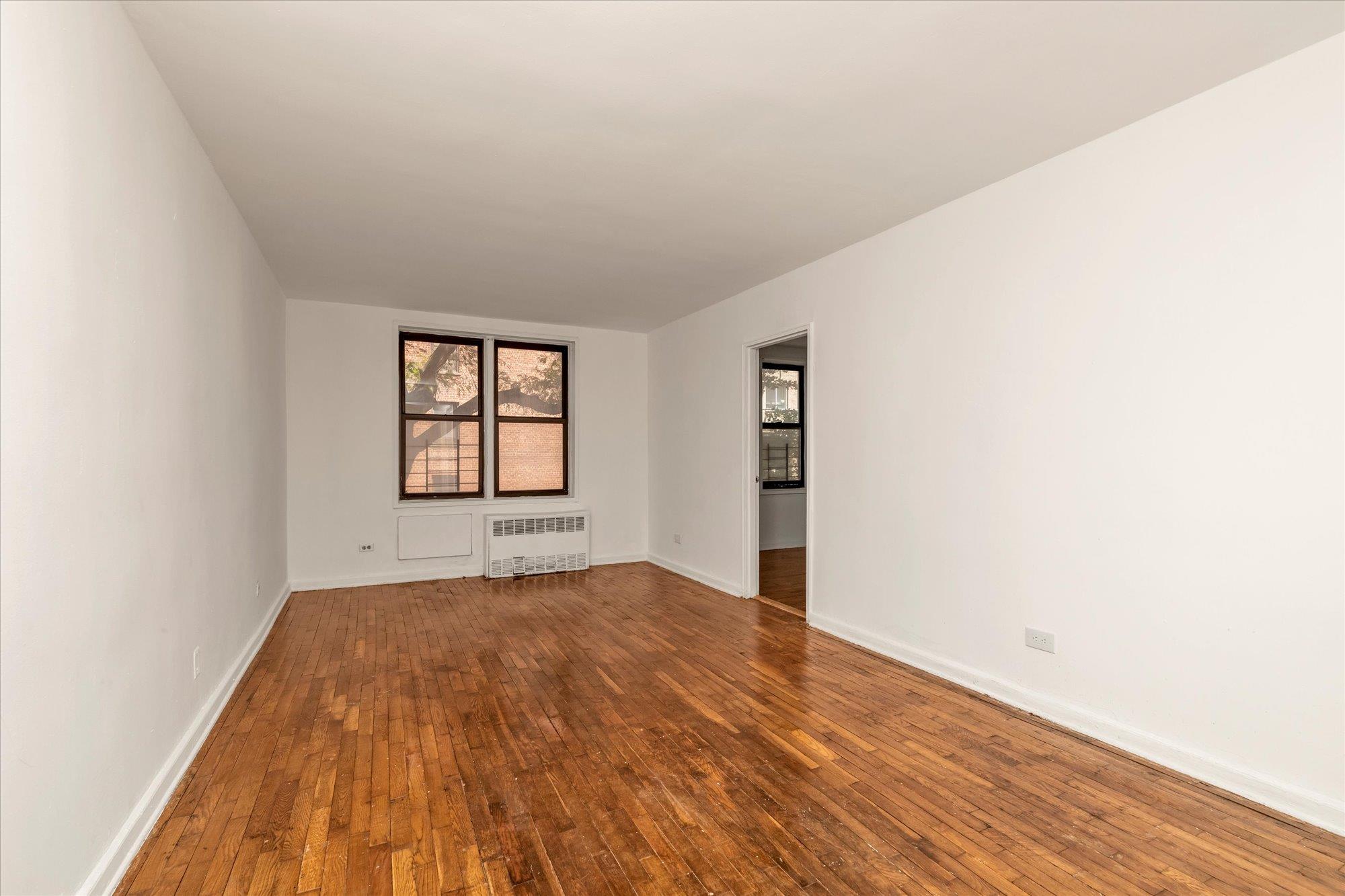 141-05 Pershing Crescent, Unit 117 Queens, NY 11435 - Photo 4 of 16 an empty room with wooden floor and windows