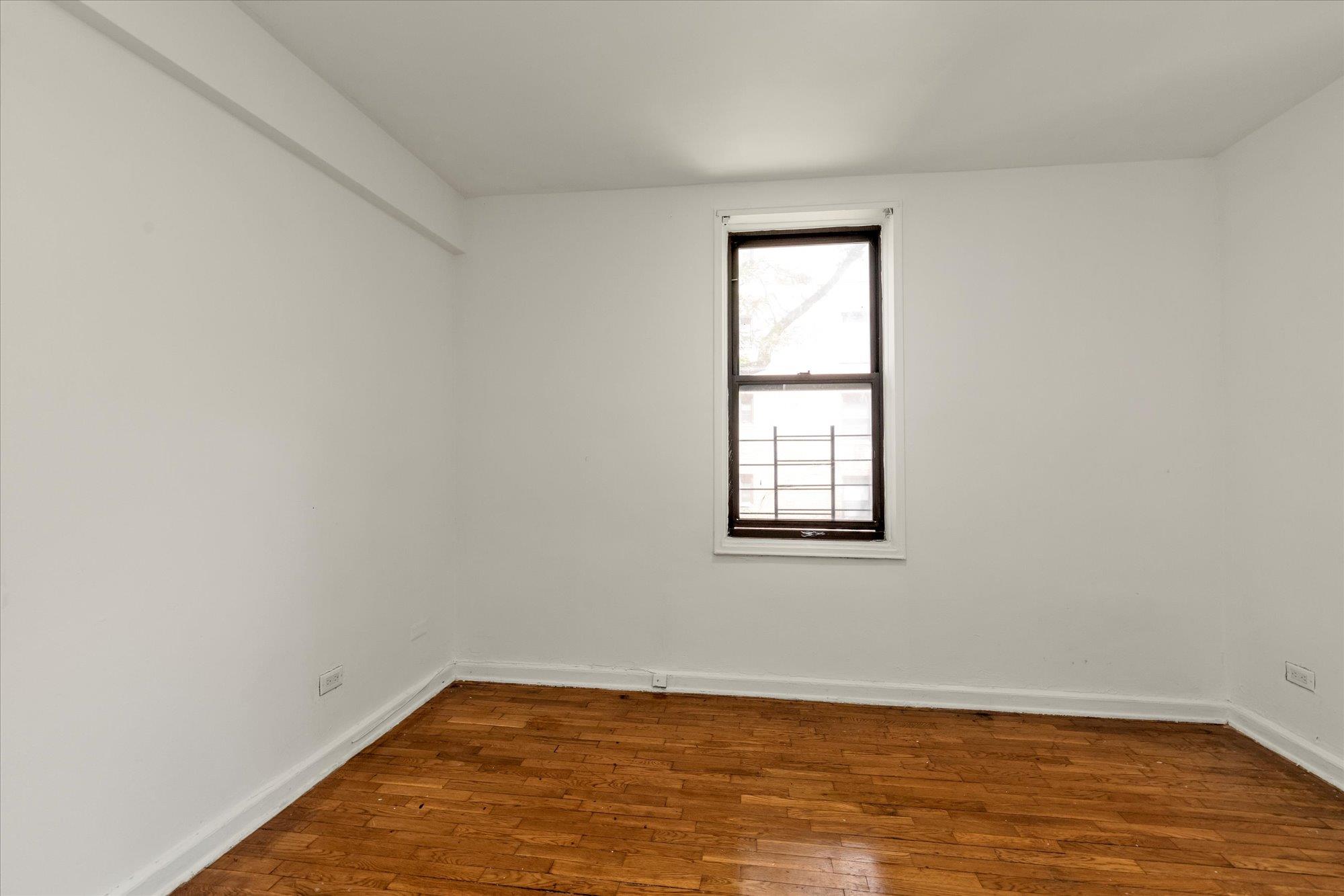 141-05 Pershing Crescent, Unit 117 Queens, NY 11435 - Photo 6 of 16 an empty room with wooden floor and windows