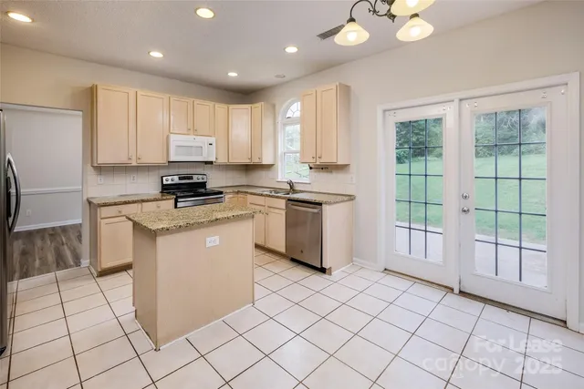 a kitchen with white cabinets a sink a stove a refrigerator and a window
