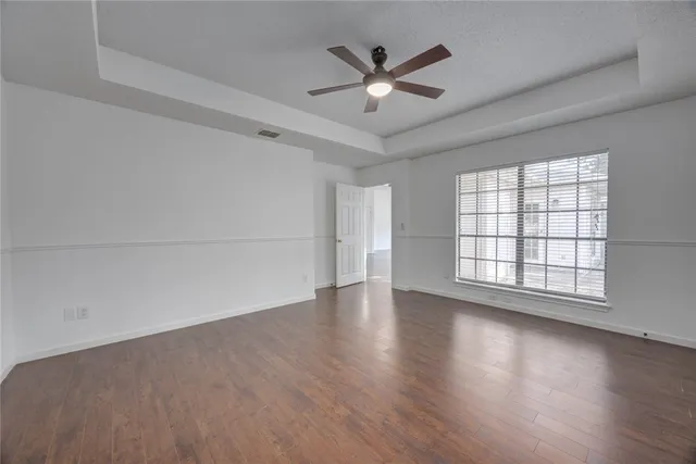 an empty room with wooden floor fan and windows